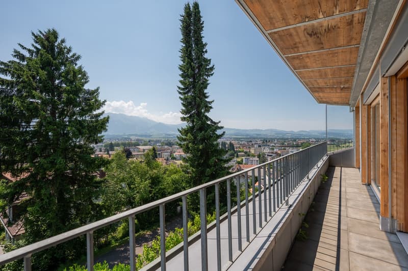 Balcony with metal railing, wooden ceiling, tiled floor, overlooking city and mountains