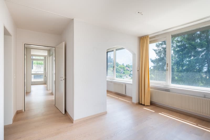 Empty room with white walls, wooden floor, large windows, yellow curtains, radiators