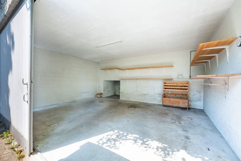 Empty garage with white walls, concrete floor, wooden shelves, and a wooden storage box.