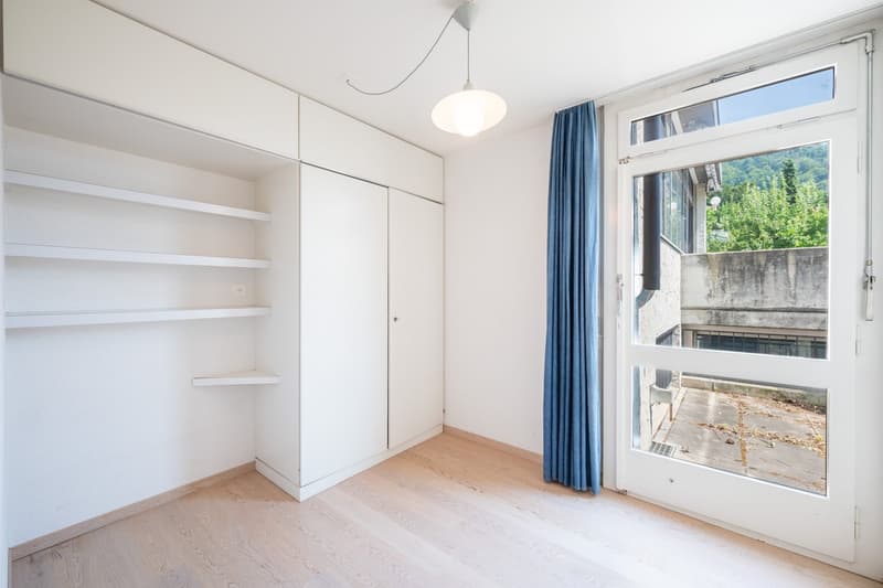 empty room, white walls, wooden floor, white built-in wardrobe, white shelves, white door, glass door with blue curtain, view of outside