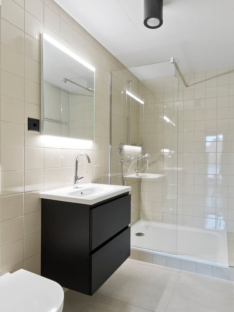 Modern bathroom with white tiles, white sink, black cabinet, and a shower stall