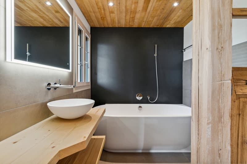 bathroom with a free standing bathtub, washbasin on wooden counter, wooden ceiling, black walls
