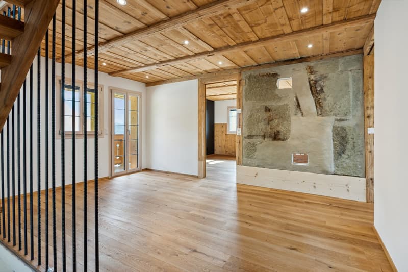 open room with wooden floors and exposed wooden beams on the ceiling, glass doors, and stone wall