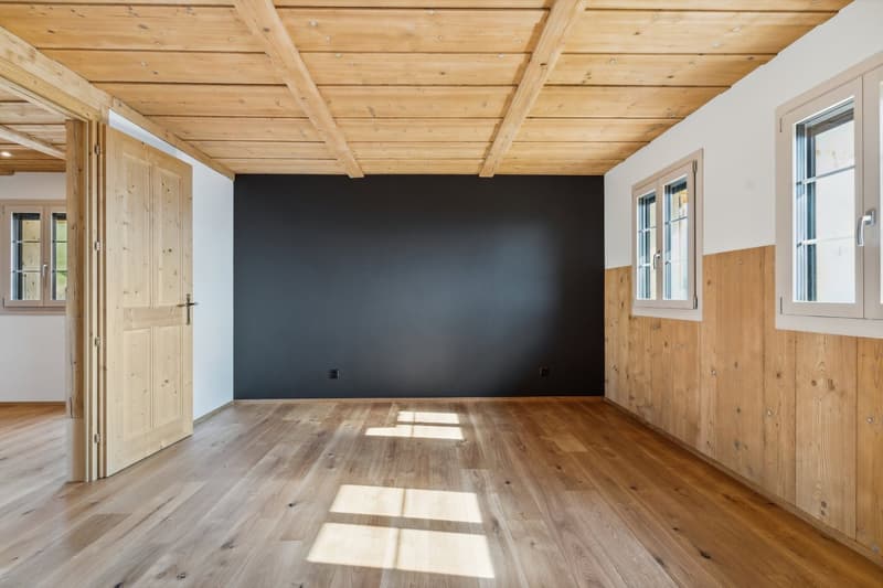 Wooden flooring, wooden exposed beams, black wall, two windows, open wooden door.