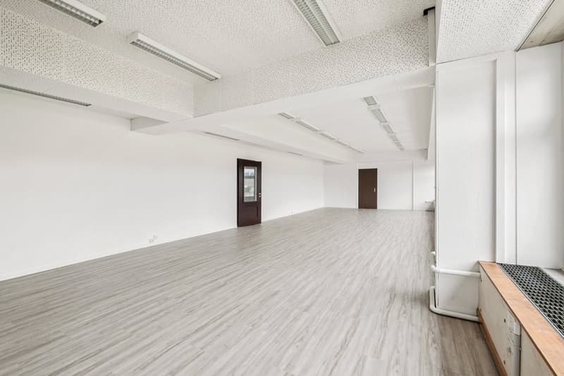 Open room with wooden floors, white walls, built-in lighting, two doors on opposite sides, two white radiators on the wall on the right