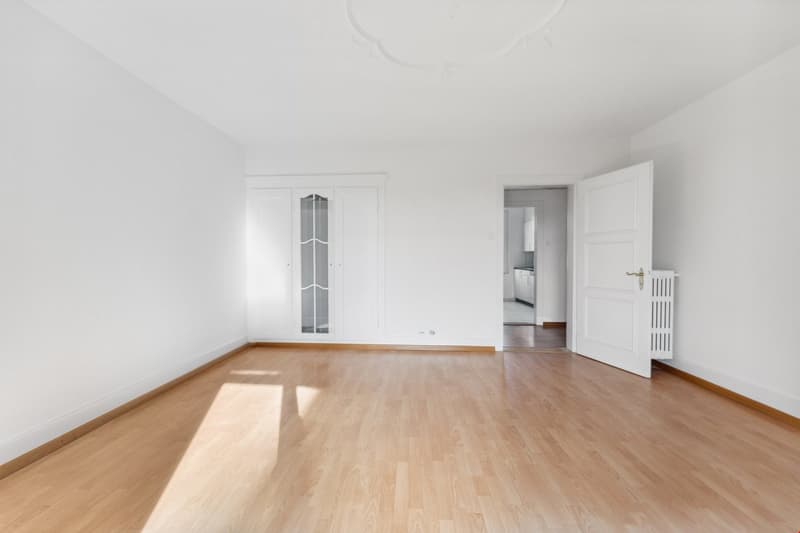 Empty room with wooden floor, white walls, two doors, and a window.