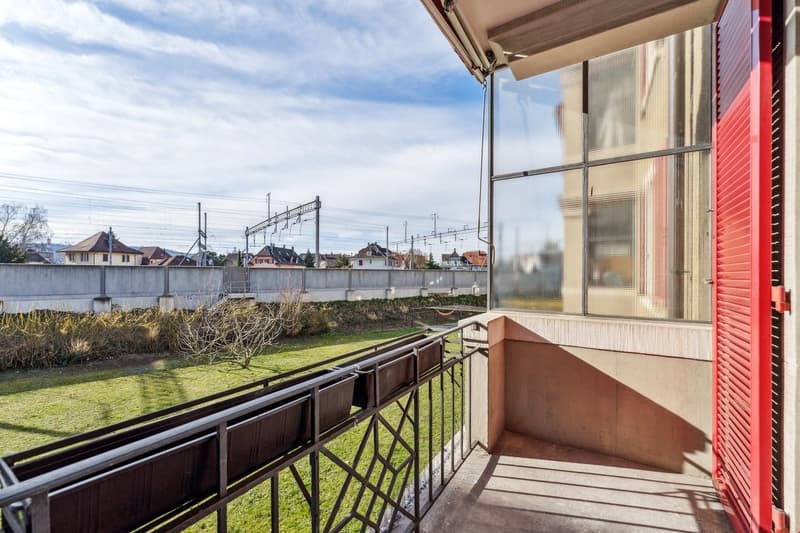 Metal railing, red shutters, balcony with view of a grassy area and a wall