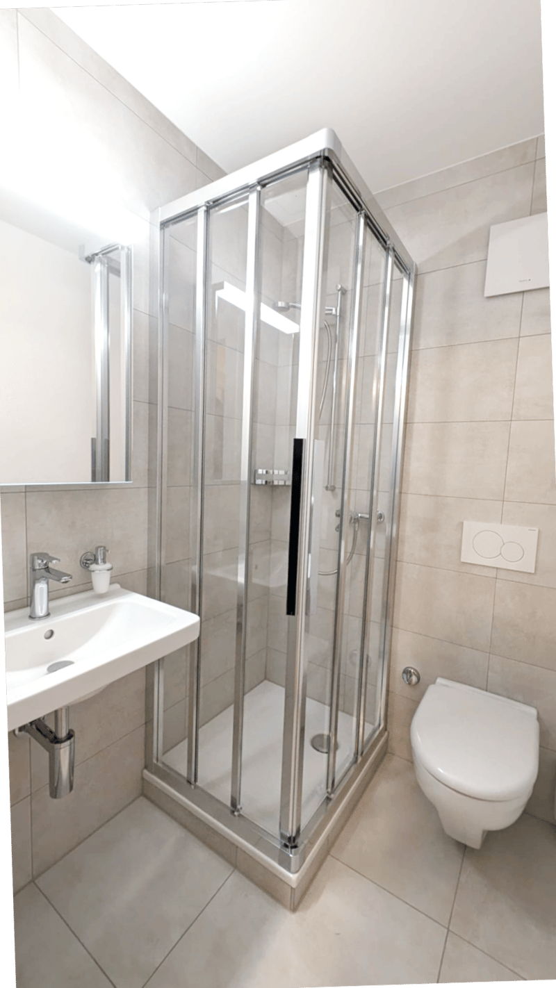 Modern bathroom with a glass shower enclosure, white sink, white toilet, and tiled floor.