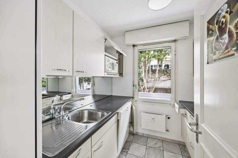modern kitchen with white cabinets, black countertops, stainless steel sink, dishwasher, microwave, and a window with a view of trees