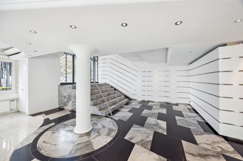 modern interior, white walls, black and white checkered floor, central column, staircase, white ceiling with recessed lighting
