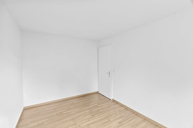 Empty room with white walls, wooden floor, and a white door.
