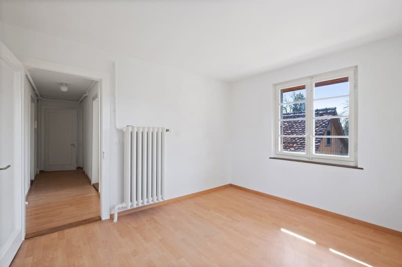 Empty room with white walls, wooden floor, white radiator, window with view outside