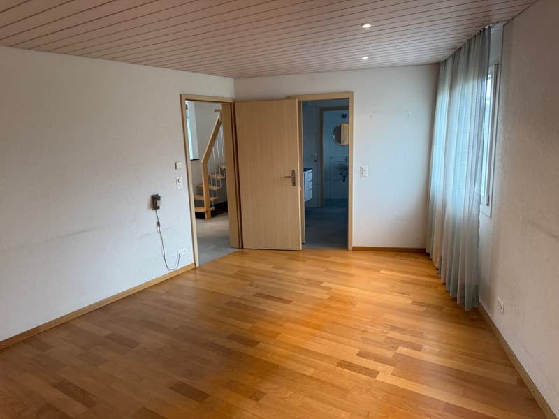 Open space with hardwood floor, white walls, power outlets, mirror in hallway, and a window with curtains.