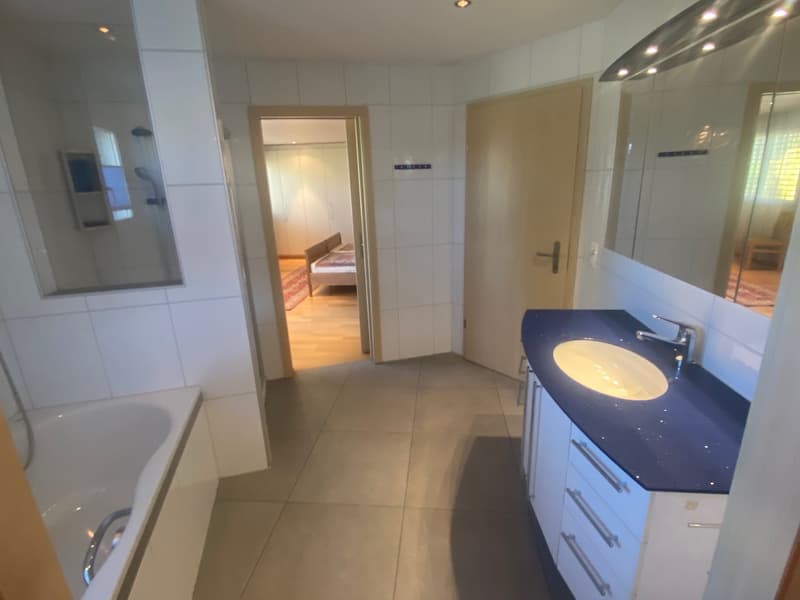 white bathtub, sink, mirror, tiled floor, white cabinets, dark countertop