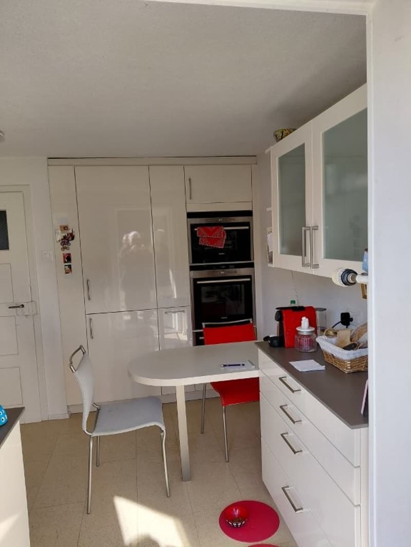 Modern kitchen with white cabinets, silver countertop, white chairs, built-in oven and dishwasher