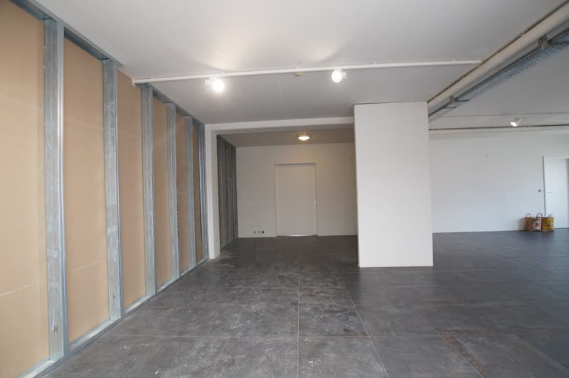 Empty room, with brown wall panels, gray tiles, a pillar, two doorways, and ceiling lights