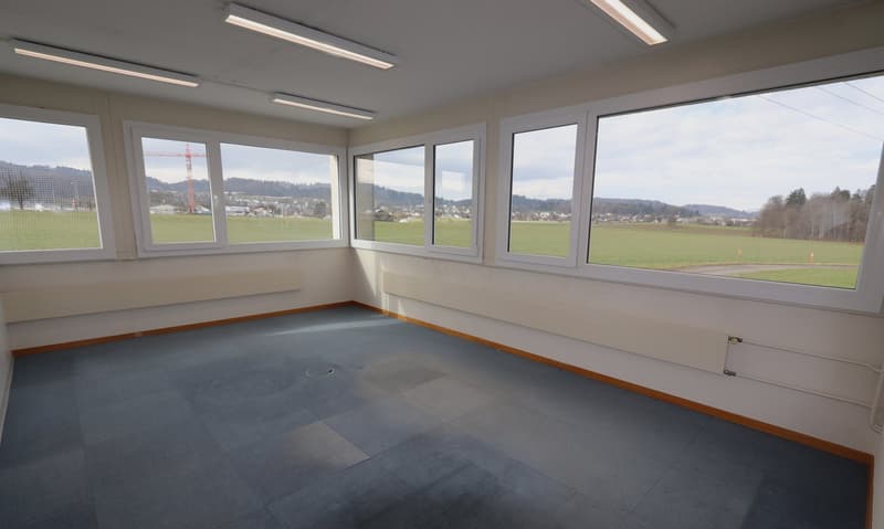 empty room with white walls, tiled floor, ceiling lights, large windows overlooking the countryside