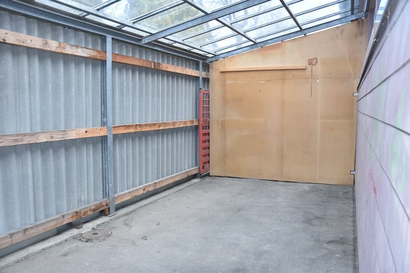 Empty garage with metal walls, wooden beams, concrete floor, and a red door.