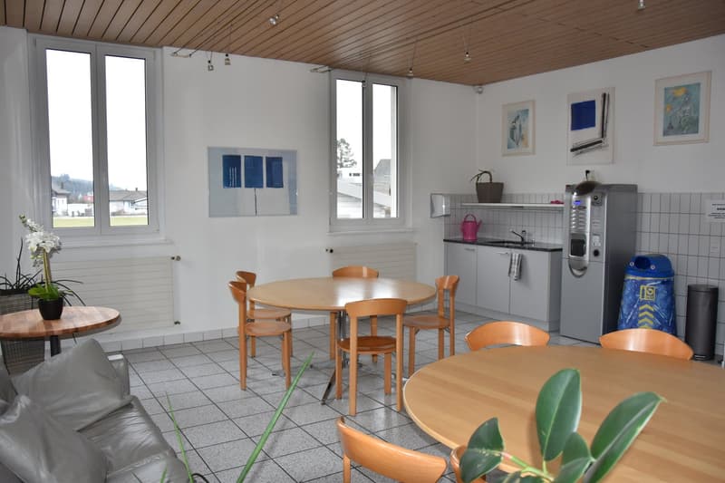 Open kitchen with dining area, wooden chairs, dining tables, couch, kitchen appliance, trash can, wall mounted radiator, and picture frames on wall