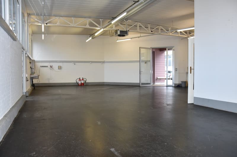 Empty room with white walls, black floor, fire extinguishers, open door, metal beams, lights