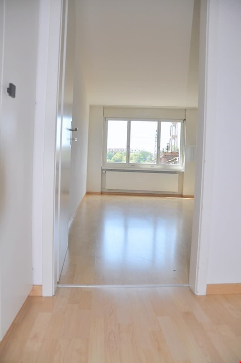Empty room with wooden floor, white walls, large window, and a white door.
