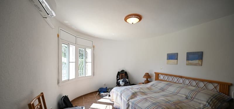 Spacious bedroom with large windows, wooden bed frame, plaid bedding, and artwork on the walls.