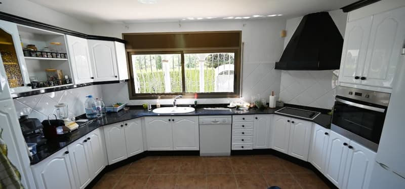 Spacious L-shaped kitchen with white cabinets, black countertops, and a large window providing a view of the outdoors. The kitchen appears to be equipped with a dishwasher and other appliances.