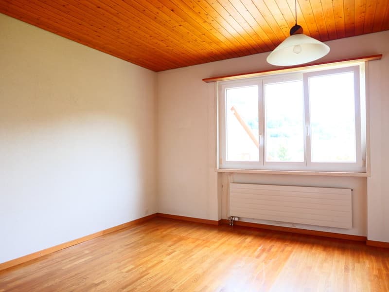 Spacious bedroom with wooden ceiling, large windows, and hardwood flooring. The room has a clean and bright appearance, with a radiator visible along the wall.