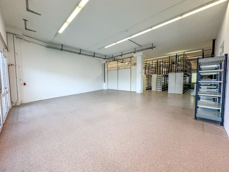 Large open space with concrete flooring, metal shelving units, and overhead lighting. The space appears to be a warehouse or storage facility.