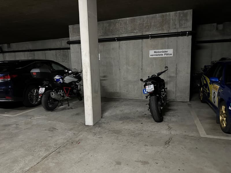 Two motorcycles parked in a parking space with concrete walls and a support pillar.