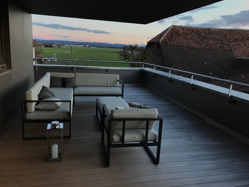 Outdoor terrace with wooden flooring, modern furniture, and a scenic view of a field and mountains.