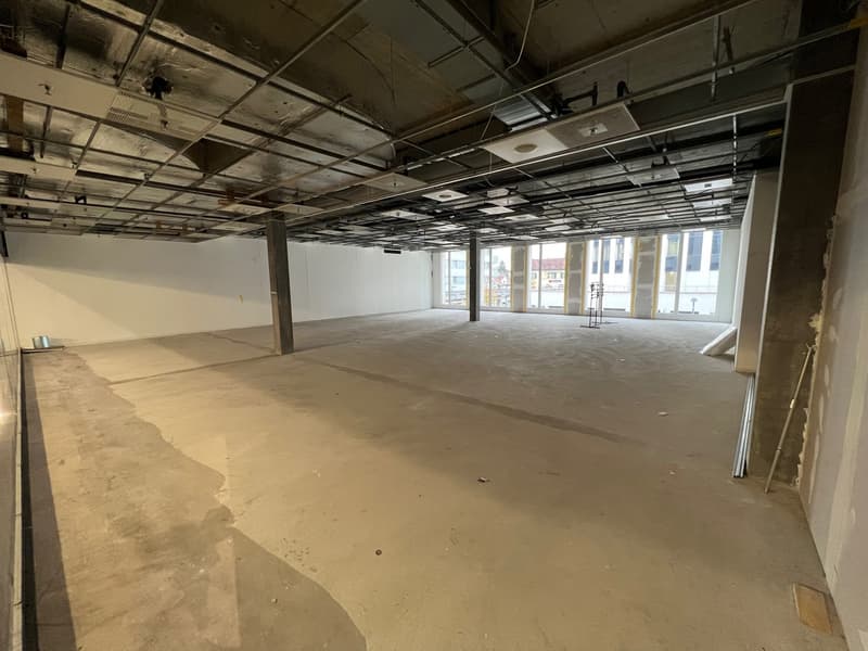 Open space with unfinished walls and ceiling, concrete floor, windows on the far wall, metal beam structures