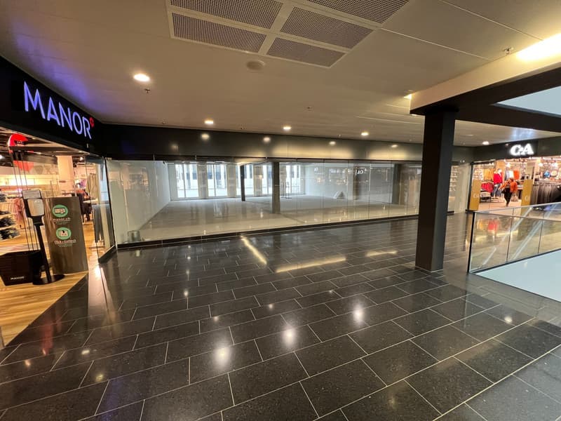 Black tiled floor, large open space, glass walls, hallway, shop signs