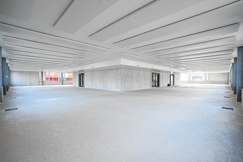 Large open commercial space with high ceilings, concrete floors, and multiple windows. The space appears to be unfinished or under construction, with exposed beams and an empty, open layout.