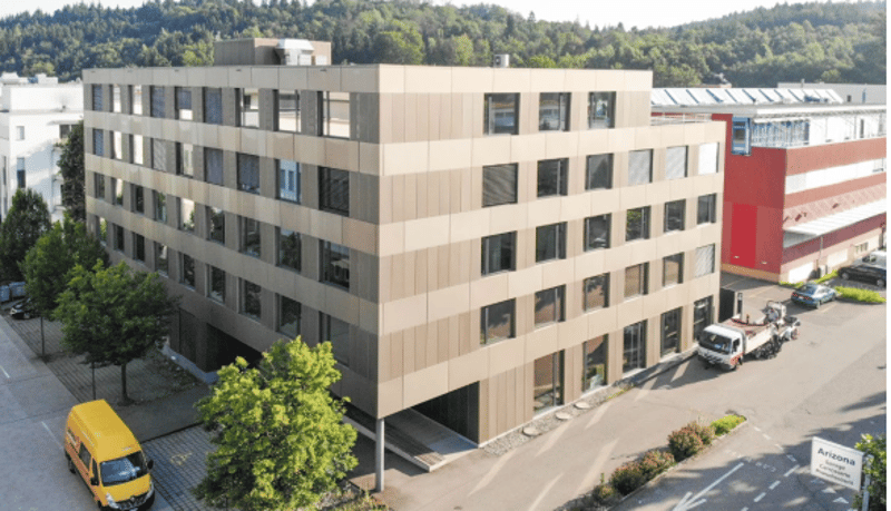 Multi-story office building with beige and red facade, windows, and parking spaces in the front