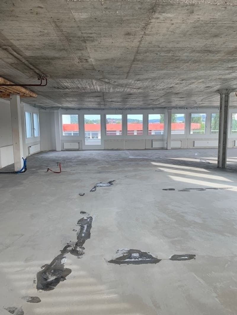 Empty room, concrete floor, white walls, glass windows, beams on the ceiling, wires on the floor.