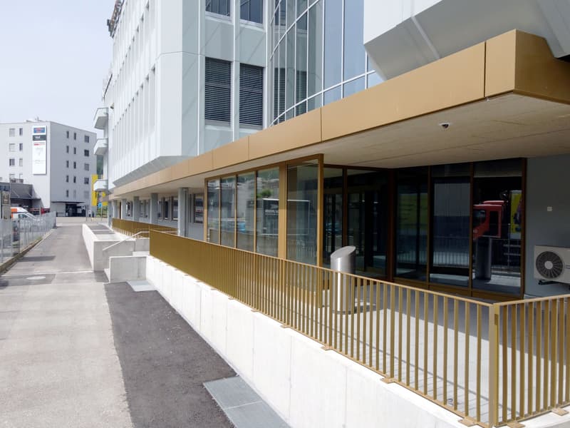 Modern office building with glass walls, gold colored railings, air conditioning unit.