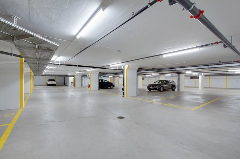 Garage, white walls, yellow lines, a few cars parked, fluorescent ceiling lights