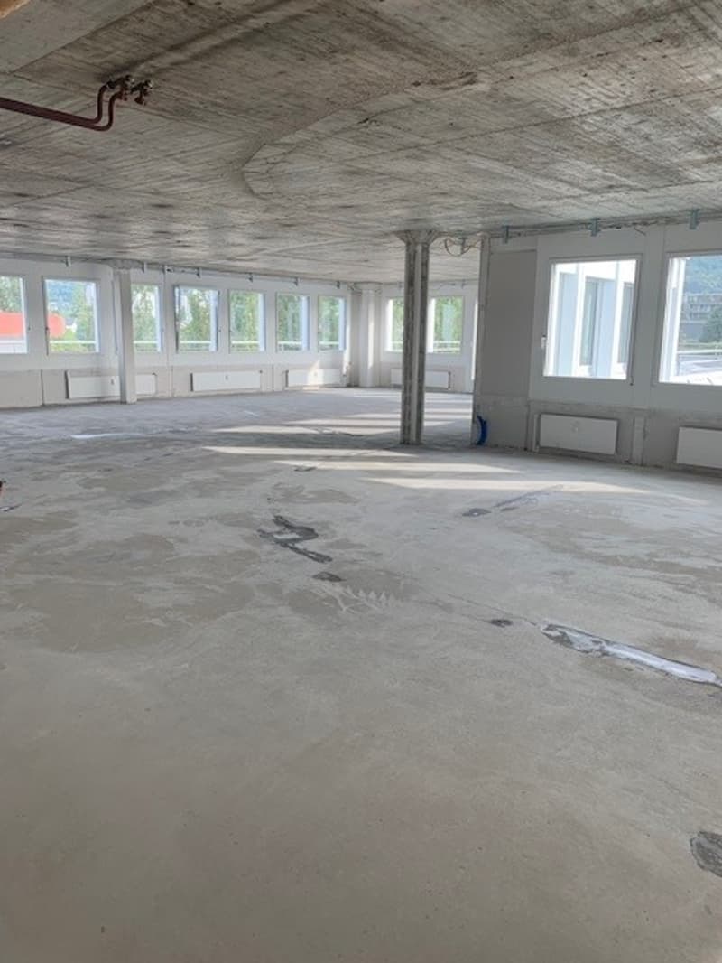 Large open room with unfinished ceiling, concrete floor, multiple large windows, central support column