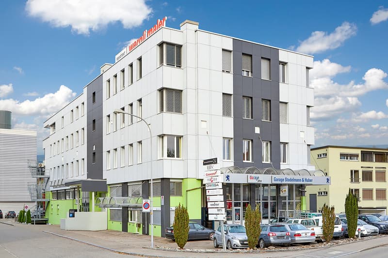5 story building, large glass windows, green accents, garage entrance, cars parked in front