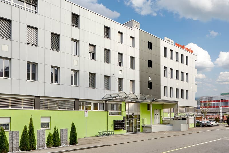 4 story white and green building, glass windows, covered entrance, 2 cars parked in front