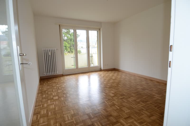 empty room, wooden parquet floor, sliding glass doors, balcony, white walls, white radiator