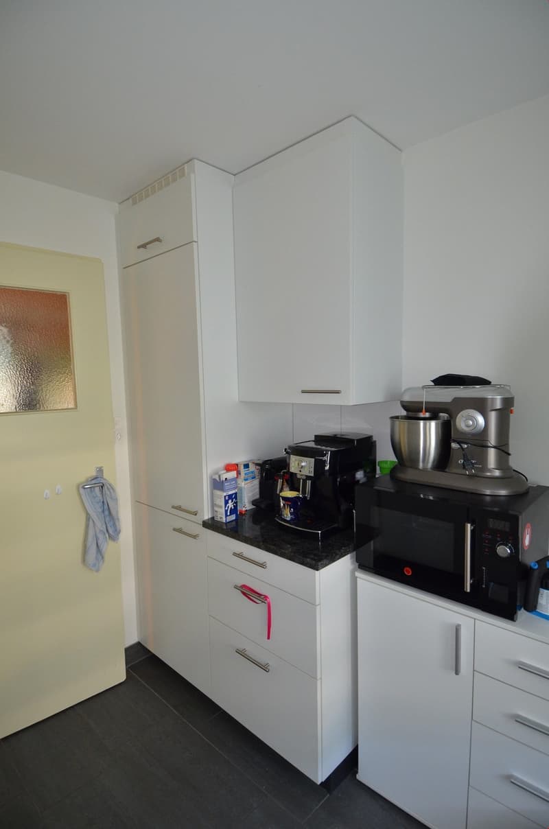 modern kitchen with white cabinets, black countertops, appliances including a coffee machine, mixer, and microwave