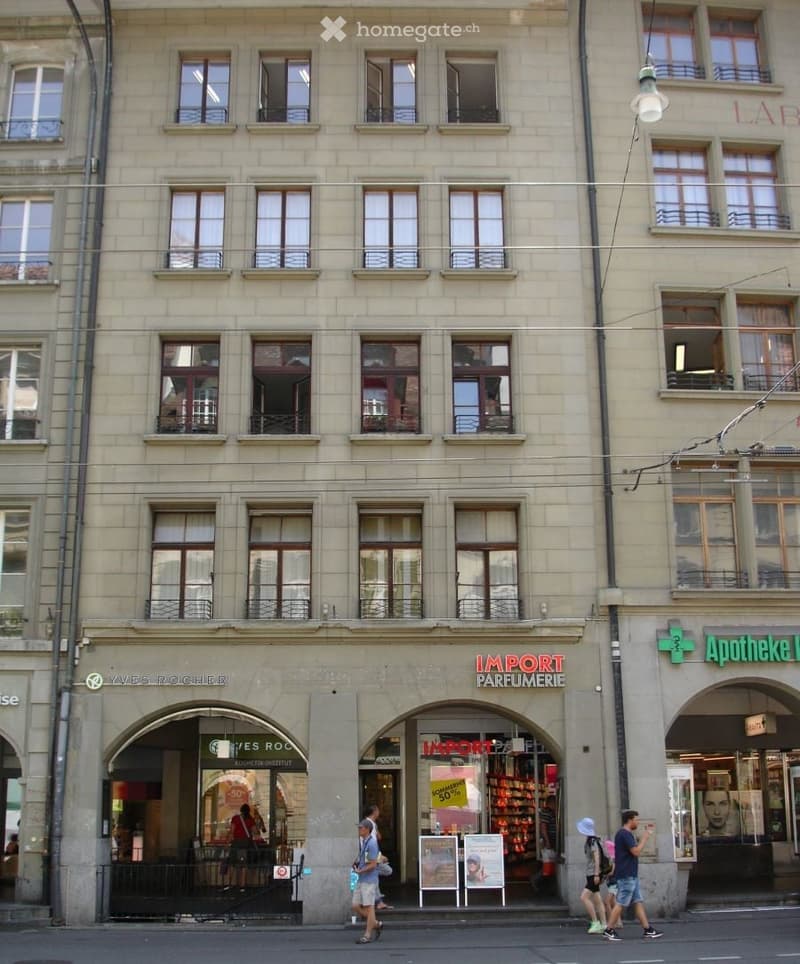 A multi-story building with multiple shops on the ground floor, large windows, and balconies on the upper floors.