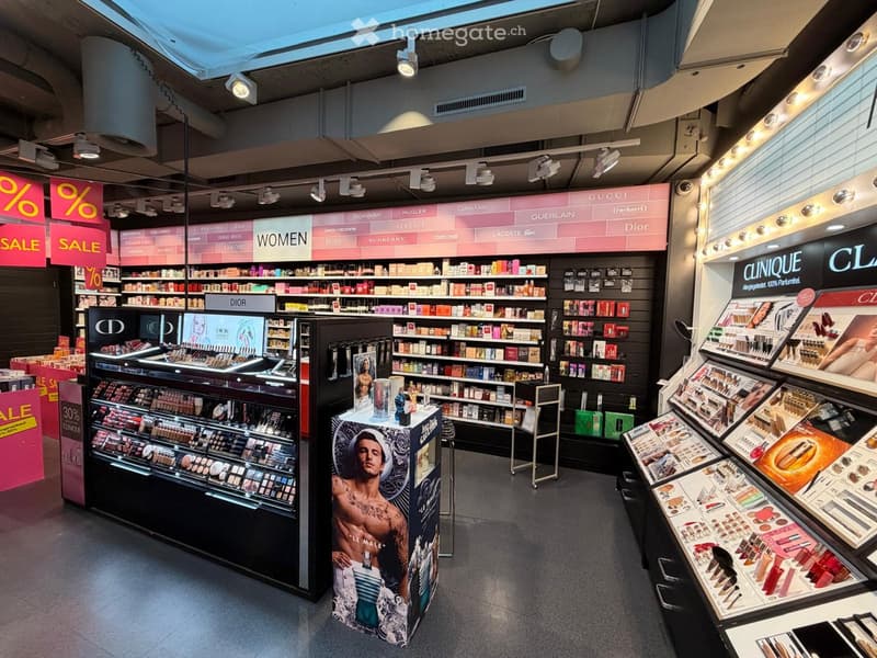 Cosmetics store with various brands displayed on shelves, illuminated by ceiling lights, sale signs, and a central display featuring a male model.
