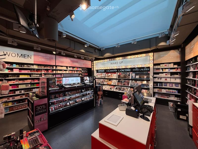 Cosmetics store with various brands displayed on shelves, a central counter with a computer, and a signboard with the text 'MAKE-UP'.