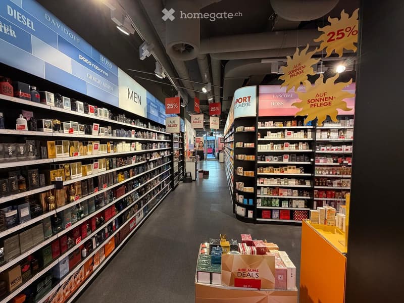 Aisle in a store with shelves full of perfume bottles, signs with discounts, and promotional items on display.