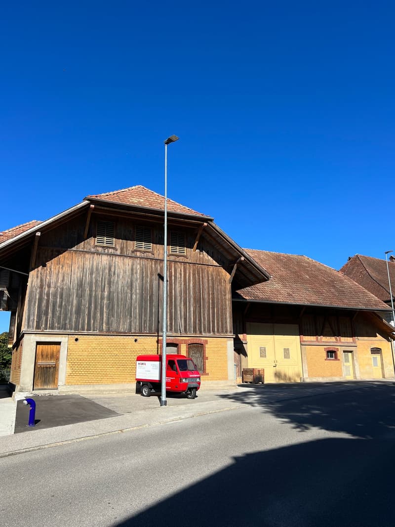 Old warehouse with brown wooden walls, red tiled roof, yellow bricks, red delivery truck parked in front