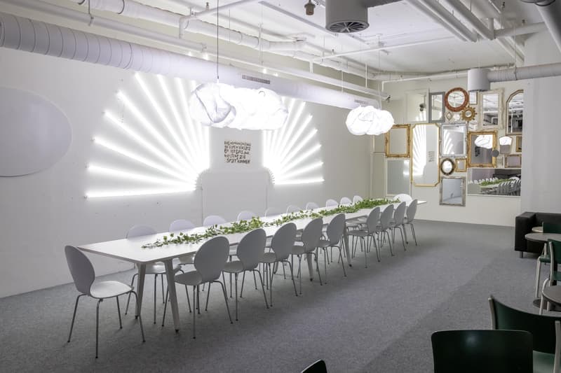 Long dining table with white chairs, carpeted floor, hanging ceiling lights, wall mirrors, black sofa, table