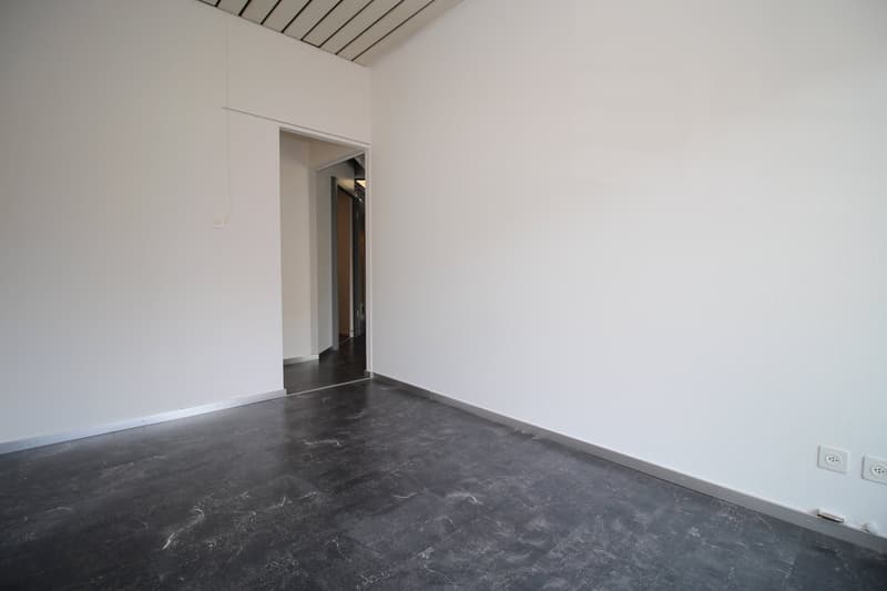 Empty room with white walls, dark gray marble-like flooring, and a doorway leading to another room.
